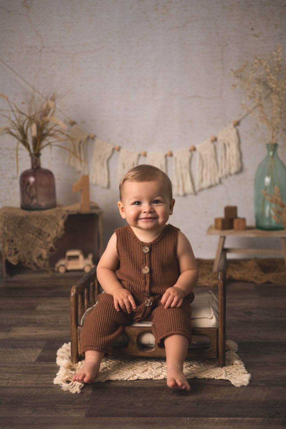 B&eacute;b&eacute; souriant en grenouill&egrave;re marron assis sur un petit lit en bois &ndash; s&eacute;ance photo b&eacute;b&eacute; &agrave; Tournai