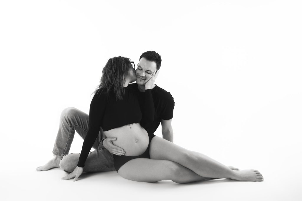 Quand faire sa séance photo de grossesse ? 1 Futurs parents enlacés sur fond blanc, le papa embrasse la future maman – séance photo grossesse à Tournai