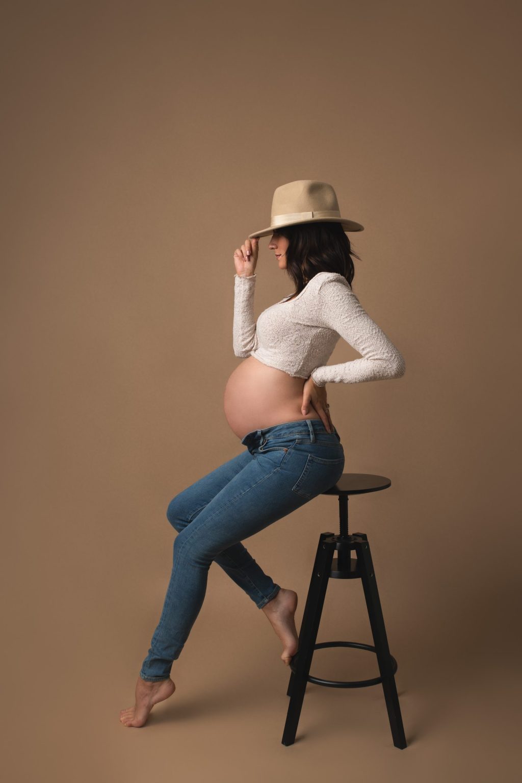 Future maman en jean et chapeau, assise sur un tabouret, ventre d&eacute;voil&eacute; &ndash; s&eacute;ance photo grossesse &agrave; Tournai
