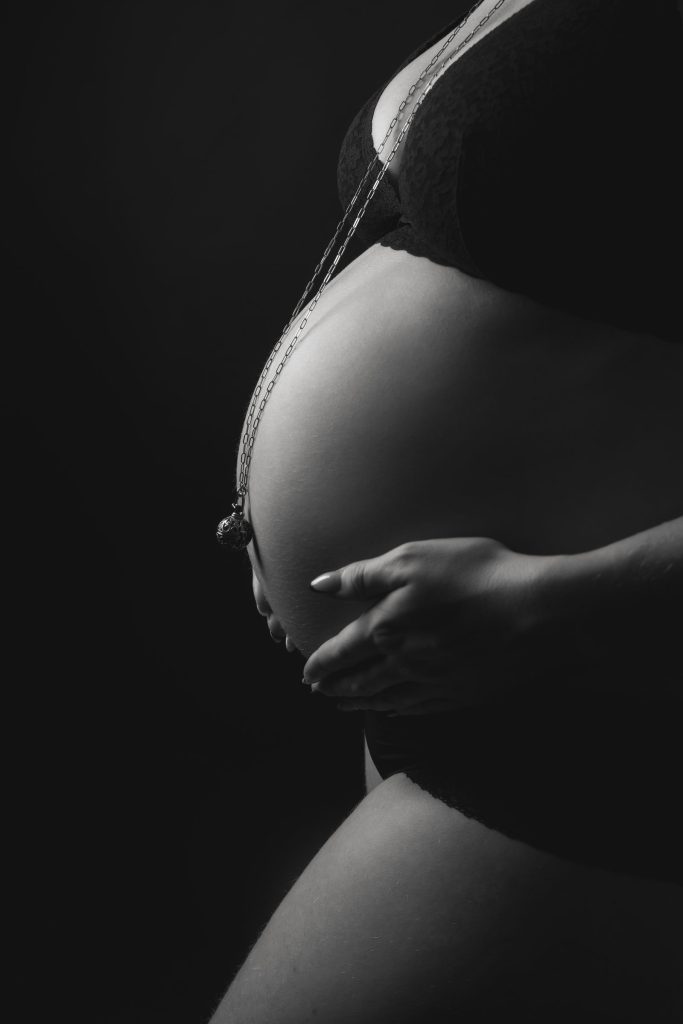Gros plan sur un ventre rond en clair-obscur, en noir et blanc &ndash; s&eacute;ance photo grossesse &agrave; Tournai